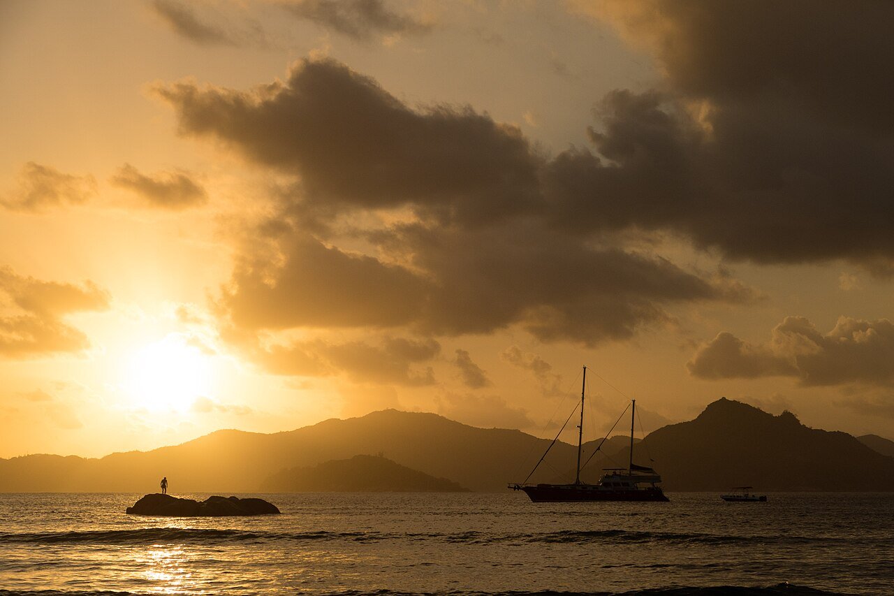 Anse Sévère La Diguella auringonlaskun aikaan, matala vesi ja graniittilohkare vasten oranssia taivasta