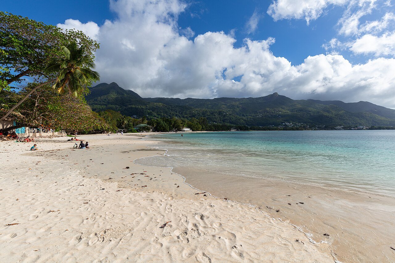 Beau Vallonin ranta ihmisineen, palmuja ja metsäiset vuoret takana