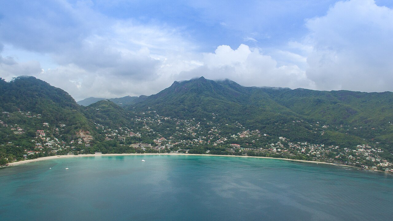 Ilmakuva Beau Vallonin lahdesta Mahéllä, pitkä hiekkakaari ja vuoret takana