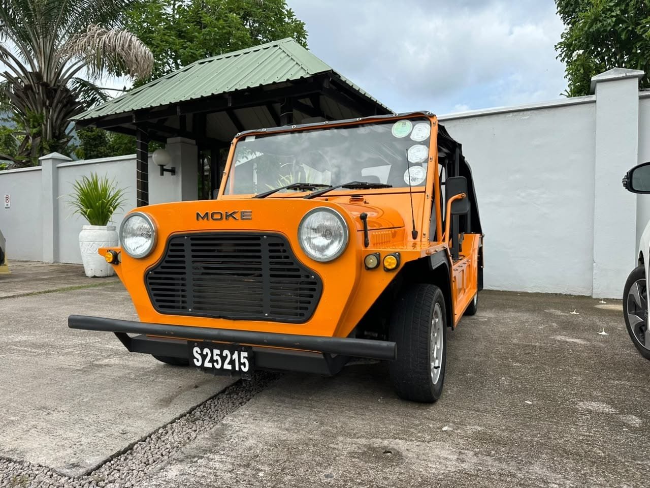 Oranssi Mini Moke pysäköitynä valkoisen huvilan portin edessä katoksen alla