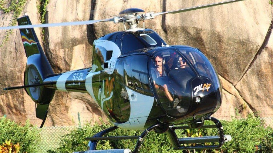 Helikopteri maassa graniittilohkareiden edessä, kaksi ihmistä ohjaamossa